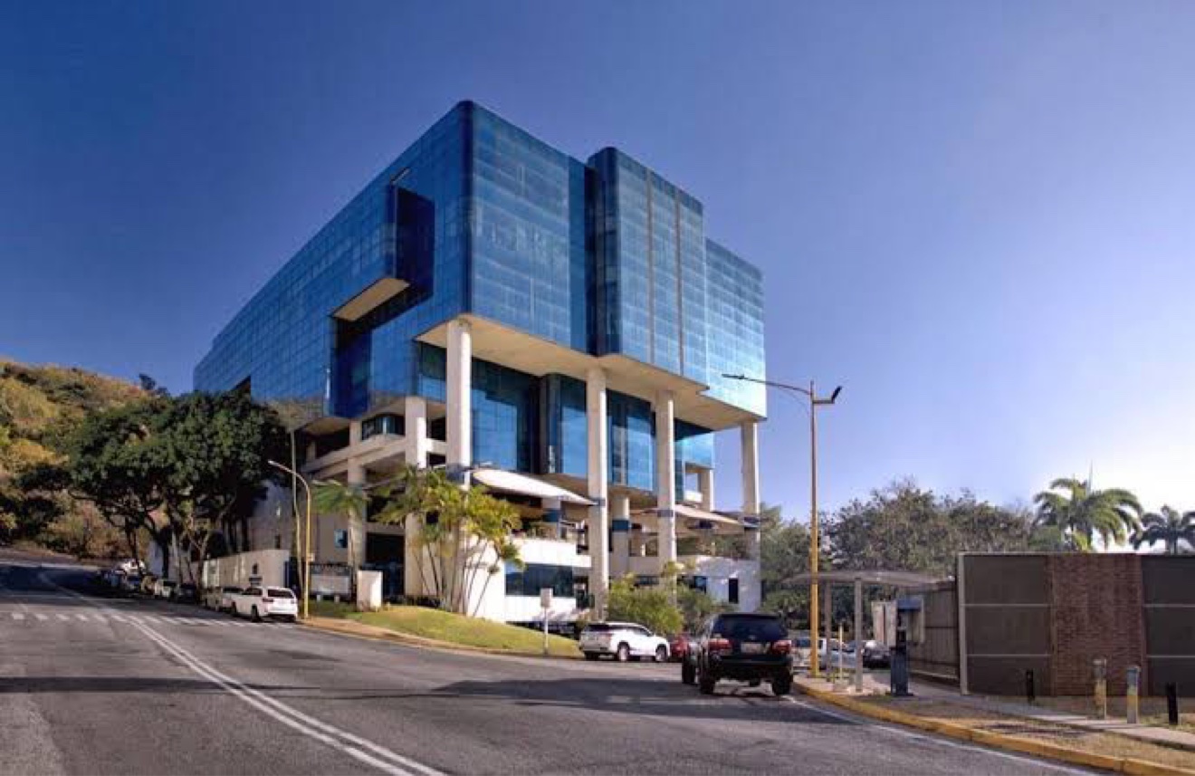 Vista real de frente del edificio del IDU desde la Calle 152 de La Viña, Valencia: la torre de vidrio azul sobre sus columnas, vista desde la calle